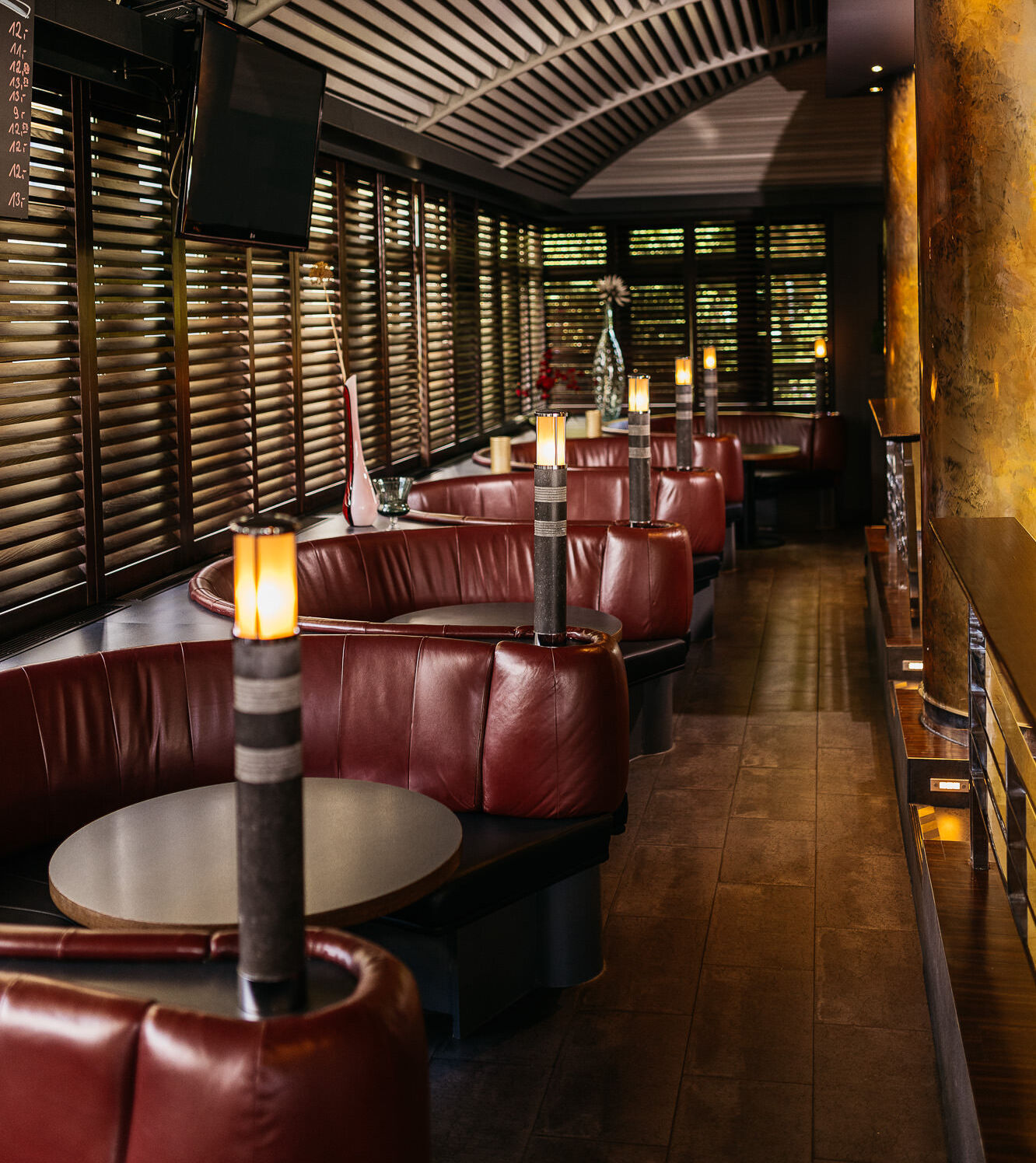 Eine Reihe von runden Lounge-Sitzecken reihen sich aneinander neben einen Gang mit goldenen Säulen.