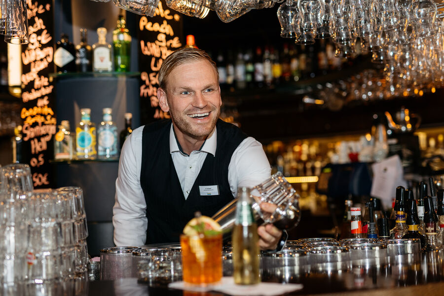 Barleiter Arndt Schlegel reicht gut gelaunt Cocktail über die Theke.